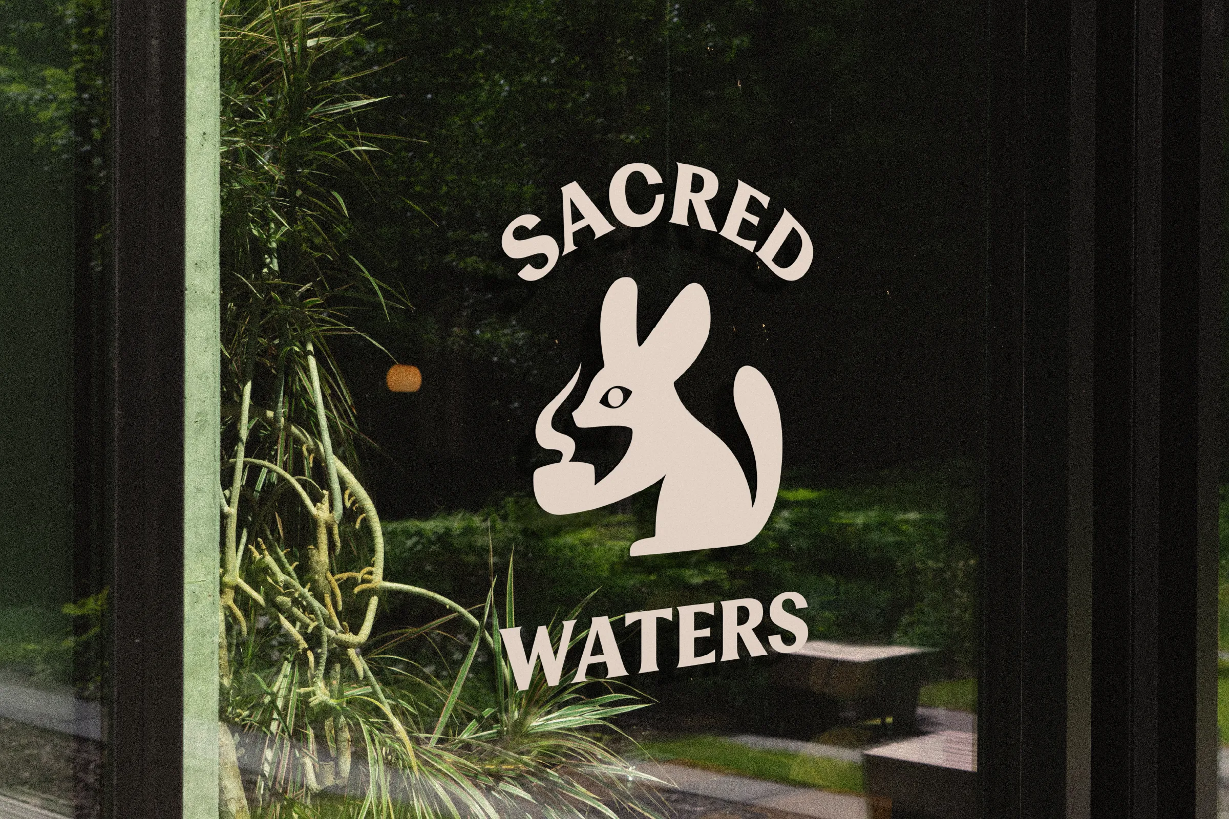 Sacred Waters fennec fox logo as a decal on a glass window with plants behind it